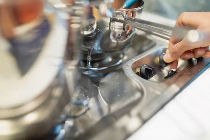 A hand adjusts a knob on a compact stainless steel sink with a dripping faucet, typical in an RV rental.. Dethleffs Just T7052 DBM 2024