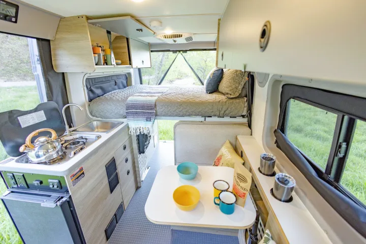 Cozy camper van interior with elevated bed, kitchenette, and dining space. Ideal rv rental for mobile adventures.. Winnebago Solis Pocket 2022