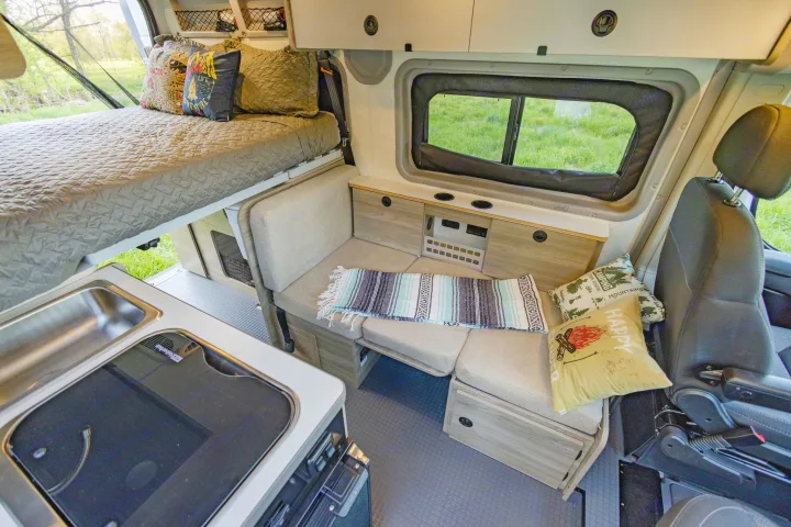 Well-equipped RV rental interior with elevated bed, compact kitchen, and lounge seating, ideal for road trip adventures.. Winnebago Solis Pocket 2022