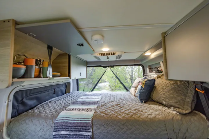 Cozy RV rental interior featuring a comfortable bed, kitchenette, and a beautiful rear window view of a serene river. Perfect for mobile adventurers.. Winnebago Solis Pocket 2022
