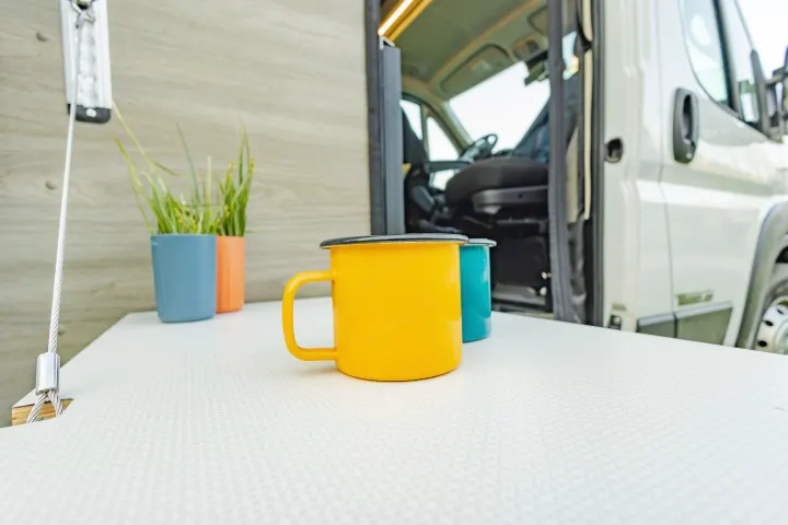 Colorful mugs on an RV rental's fold-out table, showing a cozy outdoor setup next to the camper van.. Winnebago Solis Pocket 2022