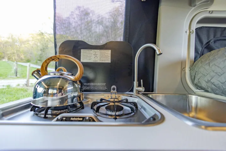 RV rental kitchen: compact stove, sink, tea kettle, with a view of nature outside from the open window.. Winnebago Solis Pocket 2022