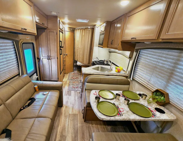 Spacious rv rental interior: sofa, dining area with green plates, kitchen, and hallway leading to rear. Well-lit & modern.. Thor Motor Coach Four Winds 2021
