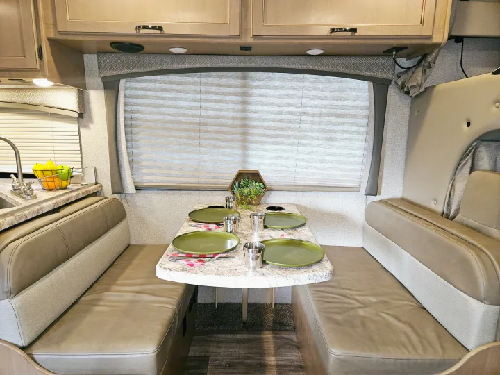 Explore this clean RV rental interior with a fully set dinette and kitchen area, ready for your road trip adventures.. Thor Motor Coach Four Winds 2021