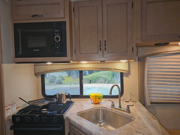 Explore comfort in this modern RV rental kitchen, featuring a microwave, stove, sink, and ample storage for your travels.. Thor Motor Coach Four Winds 2021