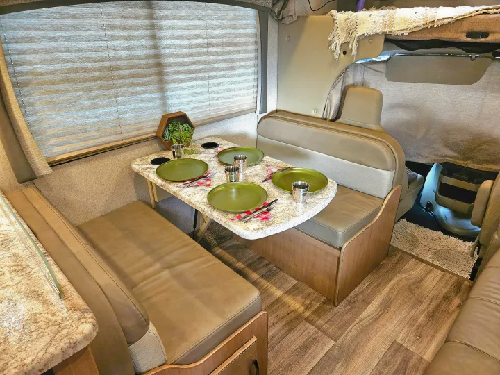 Cozy RV rental dinette with a set table, perfect for meals on the road. Features comfortable seating and wood-look flooring.. Thor Motor Coach Four Winds 2021