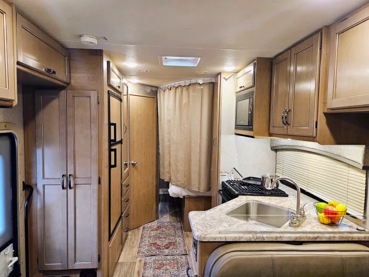 View inside an RV rental, highlighting a bright kitchen with a sink, stove, microwave, refrigerator, & wood cabinetry.. Thor Motor Coach Four Winds 2021