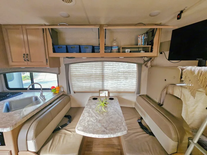 Cozy RV rental interior: A dinette with seating, kitchen with sink & stove, and organized overhead cabinets. Ideal for travel.. Thor Motor Coach Four Winds 2021