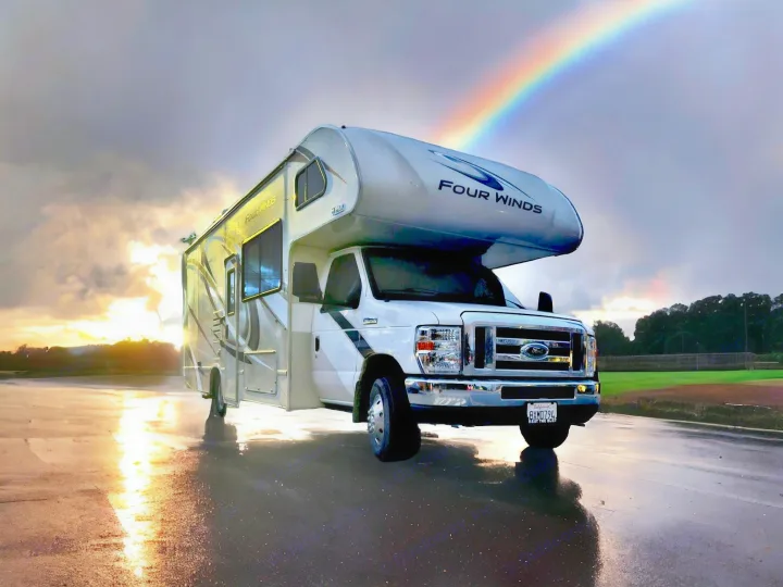 White Four Winds RV rental on a wet road with sunset reflections and a clear rainbow. Perfect for adventures!. Thor Motor Coach Four Winds 2021