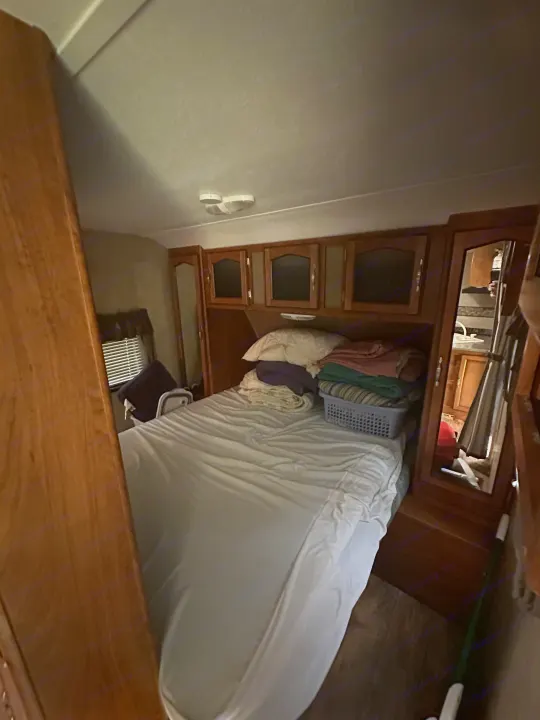 Compact RV rental bedroom showing a bed, wooden cabinets, window with blinds, and mirrored wardrobe. Ideal for travel.. Keystone RV Passport Grand Touring 2014