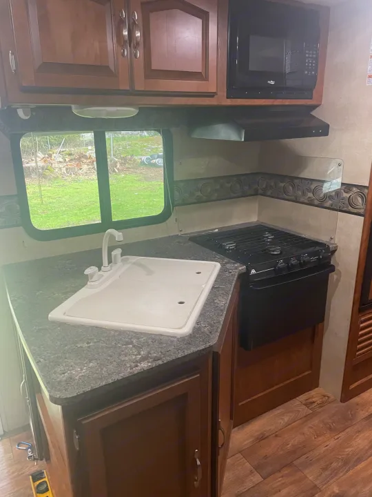 Explore this RV rental's well-equipped kitchen. Features sink, stove, microwave, and warm wood cabinetry.. Keystone RV Passport Grand Touring 2014