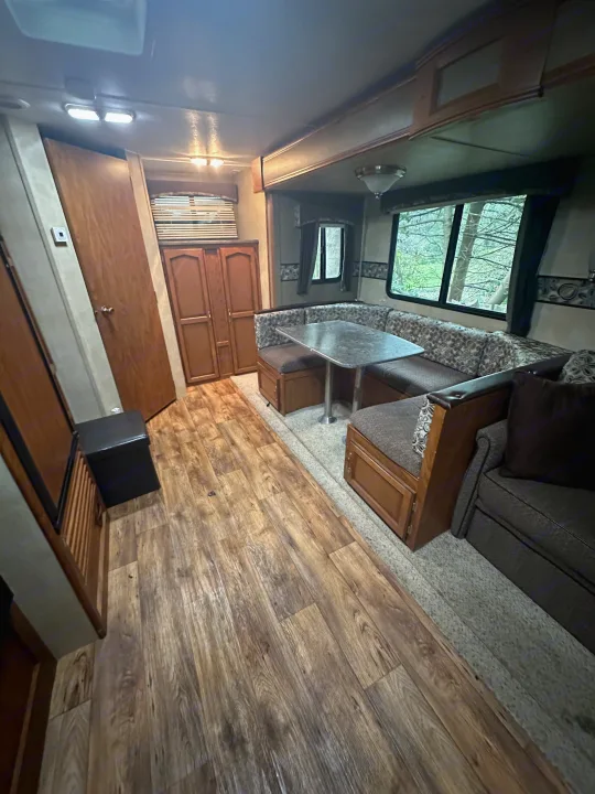 An RV rental interior showing a U-shaped dinette, sofa, and laminate wood flooring for comfortable travel.. Keystone RV Passport Grand Touring 2014