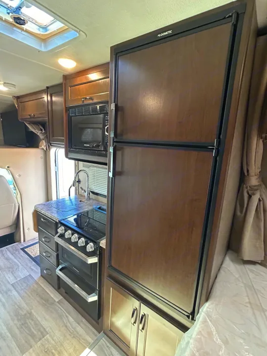 This RV rental kitchen boasts a Dometic fridge, Greystone microwave, Furrion stove/oven, sink, and wood-toned cabinets.. Thor Freedom Elite 22HE 2020