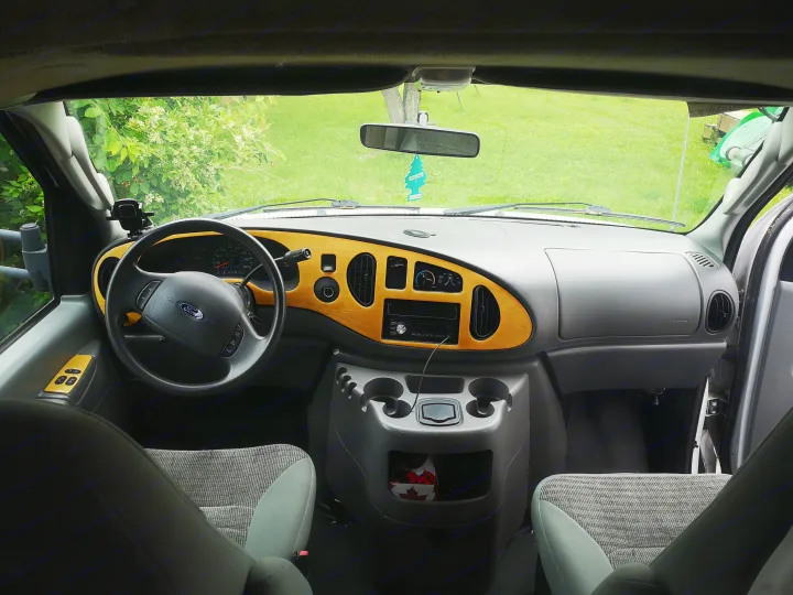 RV rental van interior: dashboard, steering wheel, and windshield view with greenery outside.. Ford F350 2003