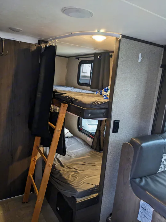 RV rental bunk beds: a cozy interior with black privacy curtains, a ladder, and a window.. Jayco Jay Flight SLX 2020