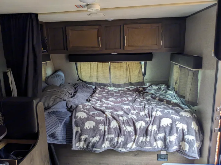 Cozy RV rental bedroom with patterned blankets, overhead cabinets, and window blinds. Ideal for adventurers.. Jayco Jay Flight SLX 2020