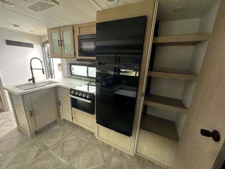 Explore this modern RV rental kitchen featuring a sink, gas stove, microwave, and tall refrigerator. Compact design with open shelves.. Forest River Salem Platinum 2024