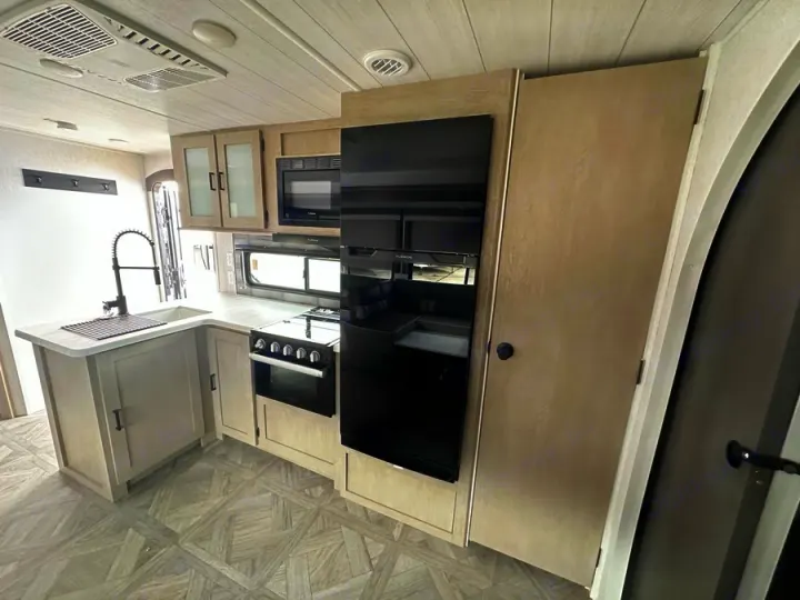 Bright RV rental kitchen features light wood cabinets, black appliances, stove, sink, and AC unit.. Forest River Salem Platinum 2024