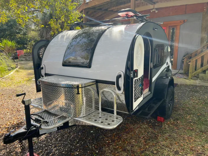 White and black teardrop camper RV rental, compact with front storage and open door, parked outdoors.. nuCamp T@G 2023