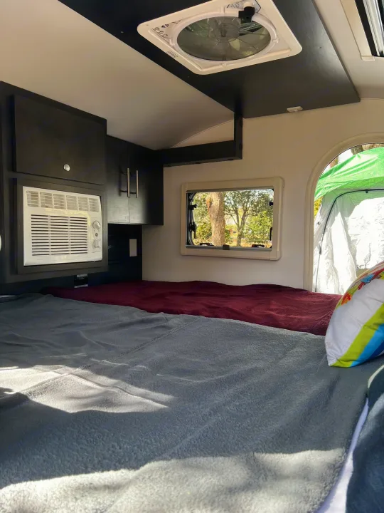 Comfortable RV rental interior with bed, AC, overhead cabinets, and a window view to nature.. nuCamp T@G 2023