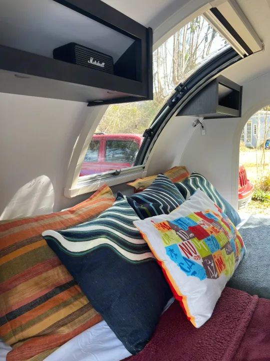 Comfy rv rental interior: colorful pillows, a Marshall speaker on a shelf, and a window view of the outside.. nuCamp T@G 2023