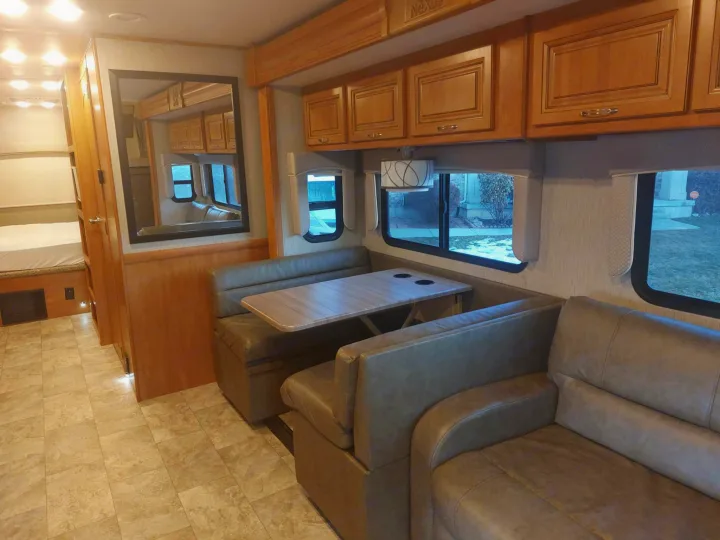 Spacious RV rental interior with dinette, sofa, overhead cabinets, and a glimpse of bunk beds on the left.. Nexus RV Wraith 2021