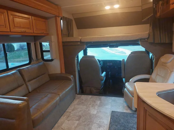 An rv rental's spacious interior: brown sofa, kitchen counter, cockpit, and overhead bunk, offering comfortable travel.. Nexus RV Wraith 2021