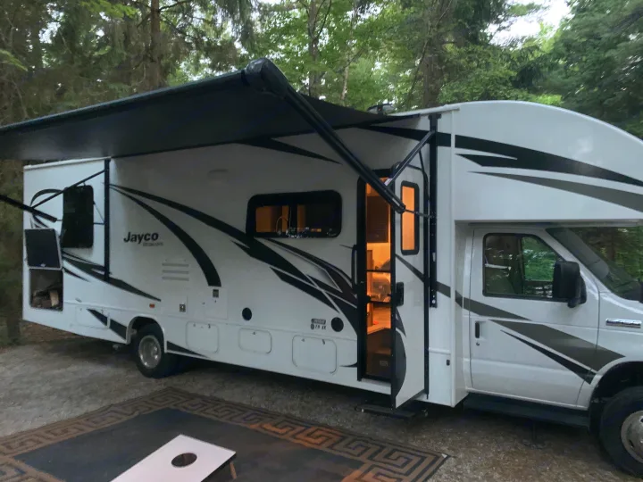Enjoy a nature escape with this Jayco RV rental. A white motorhome, awning extended, parked at a campsite with a cornhole game.. Jayco Redhawk 29XK 2023