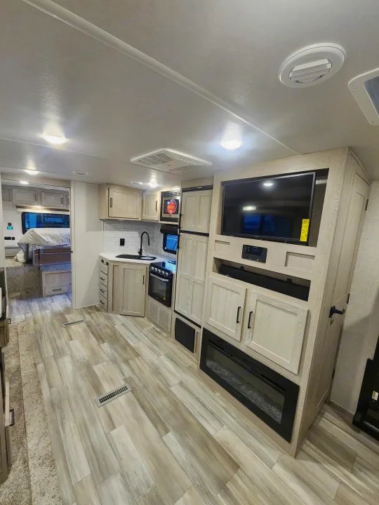 Modern RV rental interior: kitchen, living area with TV, fireplace, and bedroom visible. Light wood tones throughout.. Forest River Rockwood Ultra Lite 2022