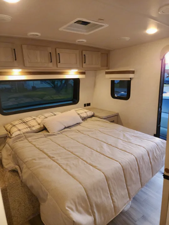 Comfortable RV rental bedroom with a large bed, overhead storage, side tables, and bright windows for a cozy retreat.. Forest River Rockwood Ultra Lite 2022