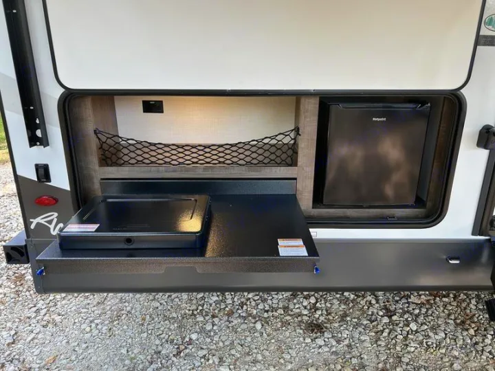 Outdoor kitchen on an RV rental with a portable stovetop, Hotpoint mini-fridge, and upper storage net for camping.. Forest River Rockwood Ultra Lite 2022