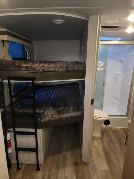 Inside an RV rental: a practical bunk bed area with ladder, and a compact bathroom with toilet and shower stall.. Forest River Rockwood Ultra Lite 2022
