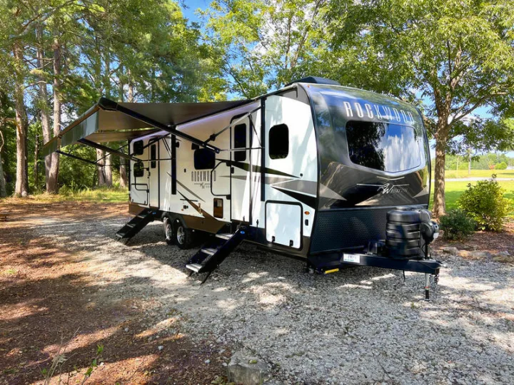 Spacious Rockwood travel trailer RV rental parked on gravel at a wooded campsite with awning extended. Perfect for your next adventure.. Forest River Rockwood Ultra Lite 2022