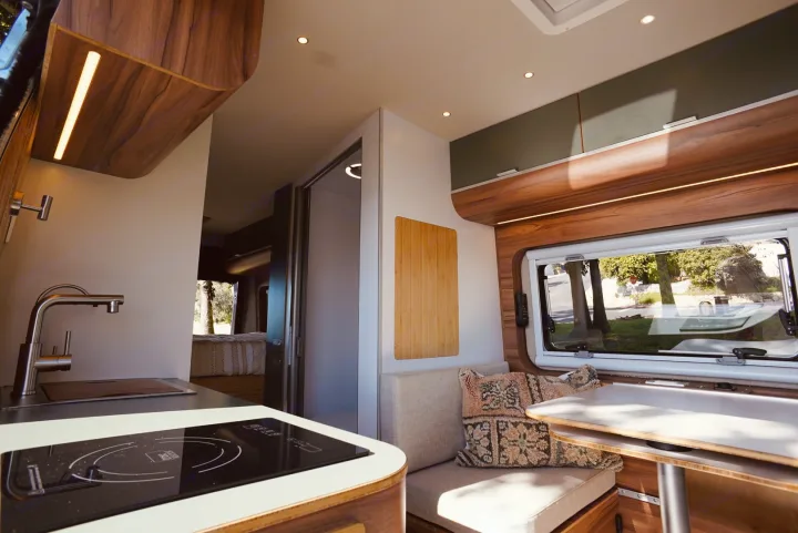 Inside a stylish RV rental: a modern kitchen with induction cooktop, cozy dining area, and bedroom beyond. Ready for adventure!. Noovo Lite 2023