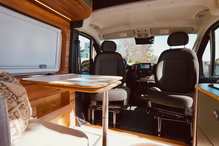 Modern RV rental interior showcasing swivel front seats, a dining table, and wood accents. Ready for road trips.. Noovo Lite 2023
