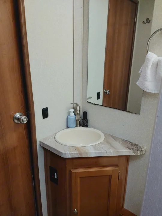 Compact RV rental bathroom with corner sink, wooden vanity, mirror, and towel rack.. Other Other 2019
