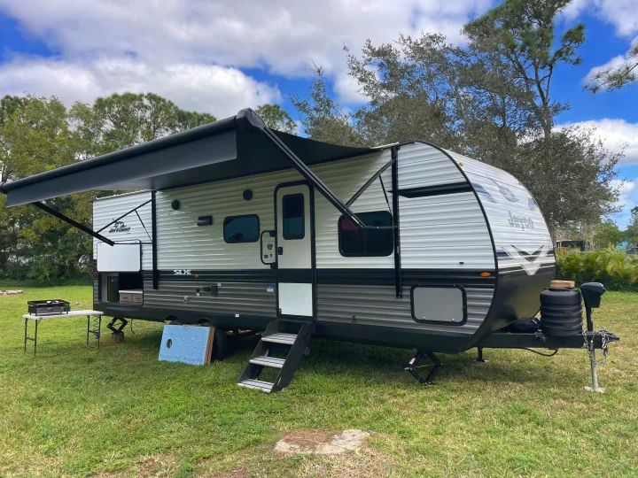This Jay Flight SLX travel trailer, perfect for an RV rental, is set up with its awning out on green grass, ready for outdoor adventures.. Jayco Jay Flight 261BHS 2024