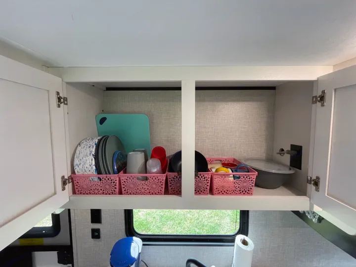 Inside an RV rental kitchen cabinet: neatly organized plates, cups, and other essentials in pink baskets, ideal for travel.. Jayco Jay Flight 261BHS 2024