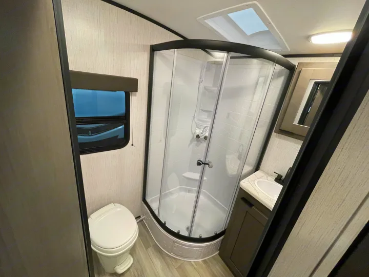 This inviting RV rental bathroom offers a space-saving corner shower, toilet, sink, window, and overhead skylight.. Cruiser RV MPG Ultra Lite 2022