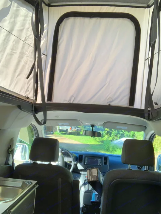 Inside an rv rental camper van, showing the front seats, dashboard, and a raised pop-top roof for travel.. NIssan Envy 2021