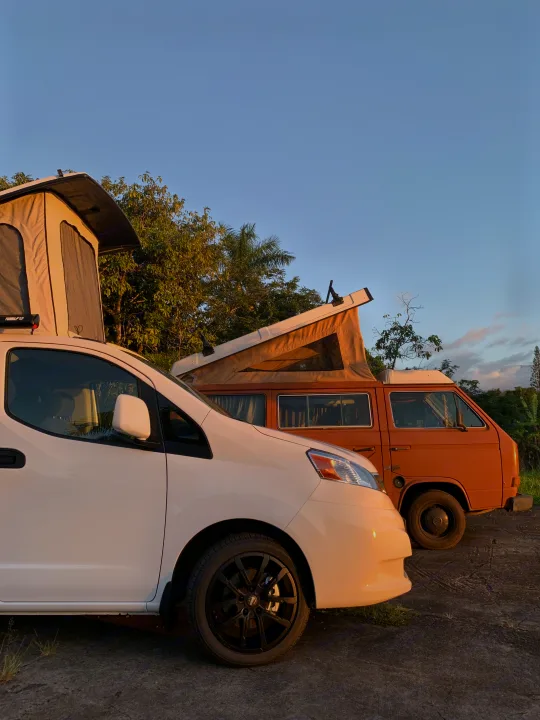 Side view of a white and an orange pop-top camper van parked outside. Explore van life with an RV rental for camping trips.. NIssan Envy 2021