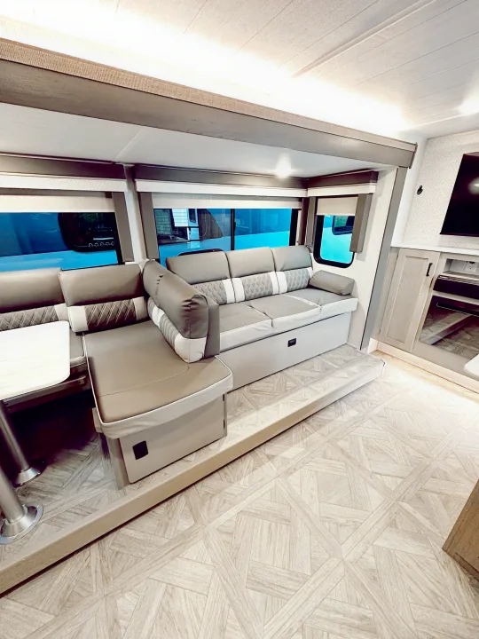 Cozy RV rental living area featuring an L-shaped gray sofa, a small table, and light wood-patterned flooring.. Forest River Wildwood X-Lite Platinum 2024