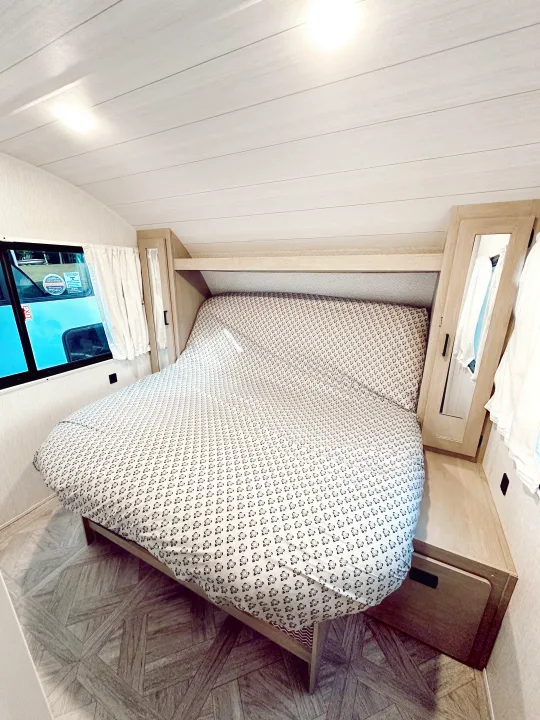 Inside an RV rental, a cozy bedroom features a patterned bed, wood cabinetry, and planked ceiling for comfortable travel.. Forest River Wildwood X-Lite Platinum 2024