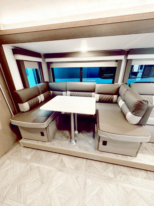 This RV rental features a cozy U-shaped dinette with brown and gray seating, a light-toned table, and geometric flooring.. Forest River Wildwood X-Lite Platinum 2024