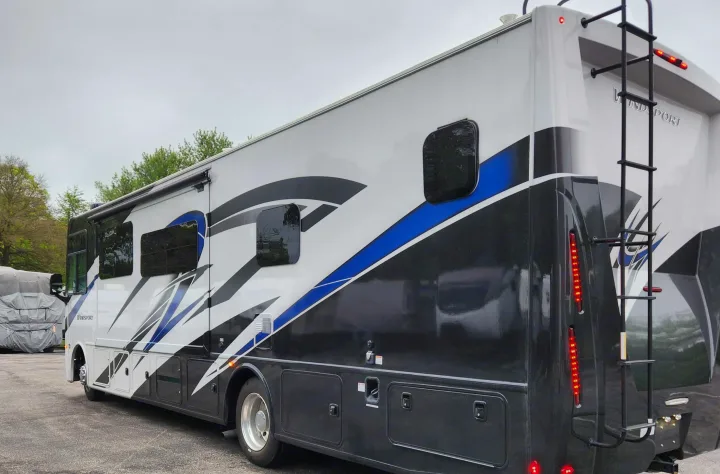 This white, black, and blue RV rental, featuring an awning and rear ladder, is parked and ready for its next adventure.. Thor Windsport 2023