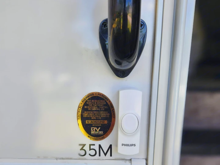 Close-up of an RV rental motorhome door, featuring a safety certification and a Philips doorbell.. Thor Windsport 2023