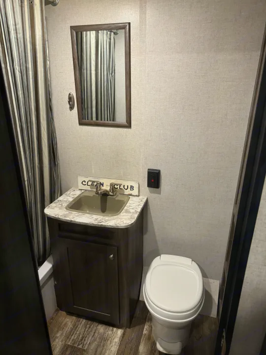 An RV rental bathroom, compactly designed with a striped shower curtain, vanity sink, mirror, and toilet.. Starcraft Autumn Ridge Outfitter 2020