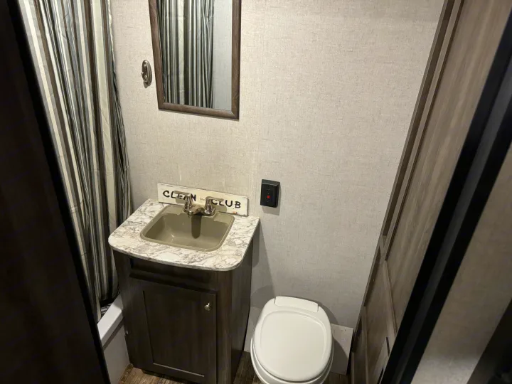 Compact RV rental bathroom with a sink, toilet, mirror, and striped shower curtain, perfect for travel.. Starcraft Autumn Ridge Outfitter 2020