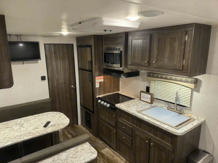 Modern RV rental interior with kitchen (microwave, stove, fridge), dining booth, and TV.. Starcraft Autumn Ridge Outfitter 2020