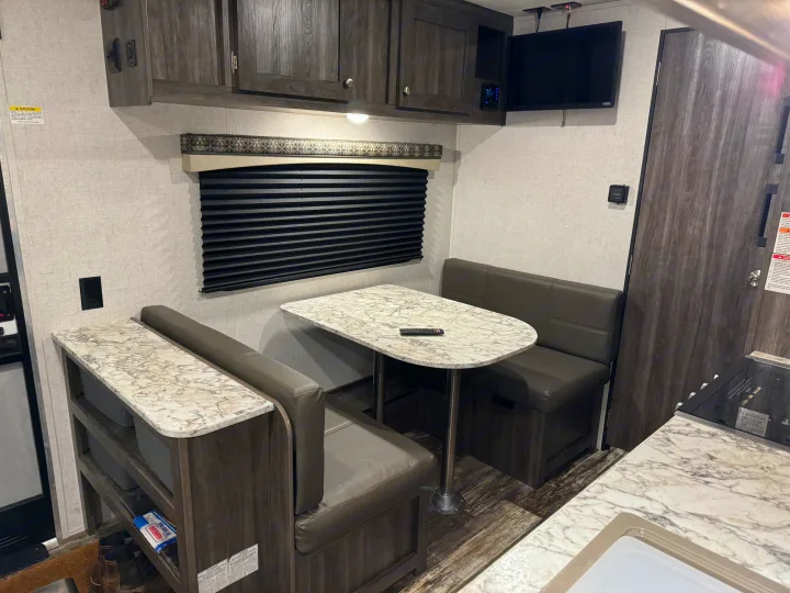 Enjoy this inviting RV rental dinette setup, featuring a faux marble table, comfy benches, dark wood cabinets, and TV for your travels.. Starcraft Autumn Ridge Outfitter 2020